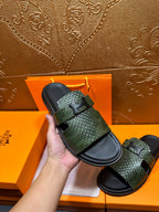 Hermes slide sandals with green textured straps and black footbeds, hand holding one