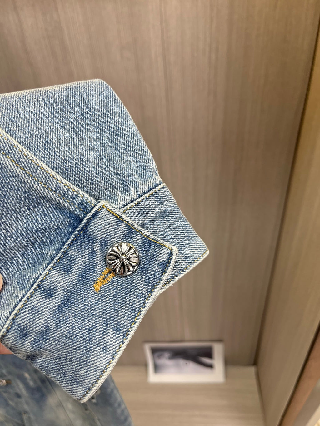 Light blue denim jacket sleeve cuff with gold button and small floral emblem