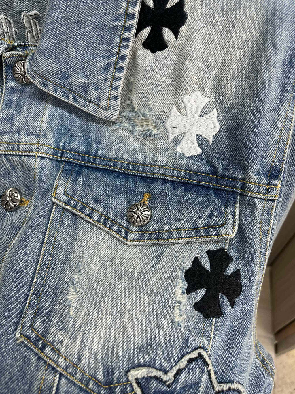 Light blue denim jacket pocket detail with gold button and black flower patches