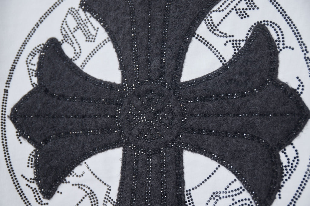 Close-up of black cross emblem with dotted trim on a white T-shirt