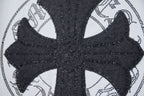 Close-up of black cross emblem with dotted trim on a white T-shirt