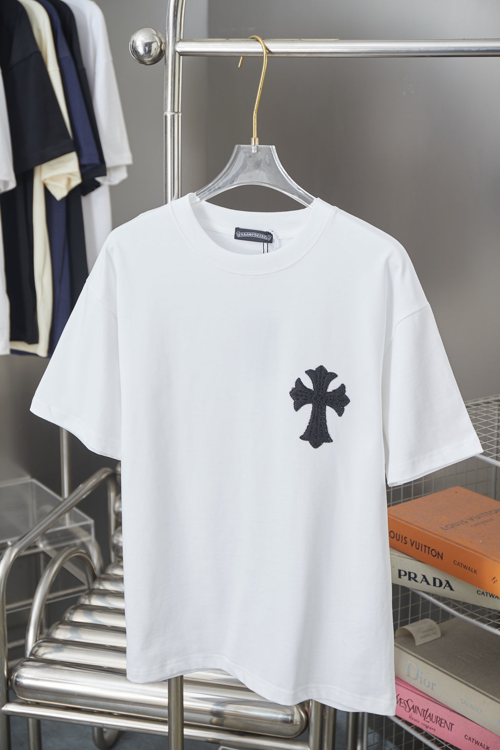 White graphic T-shirt with small black cross emblem on the chest