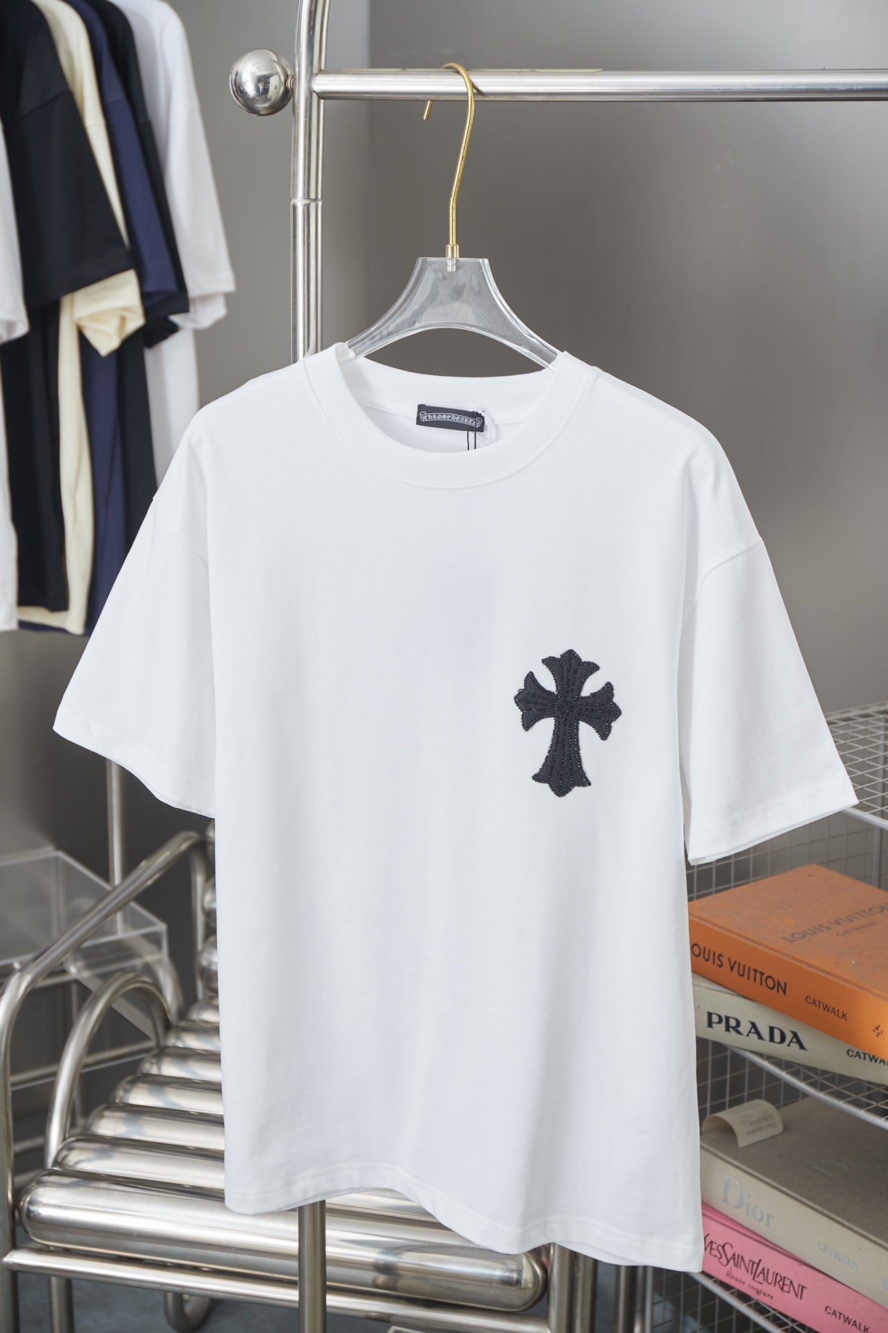 White graphic T-shirt with small black cross emblem on the chest