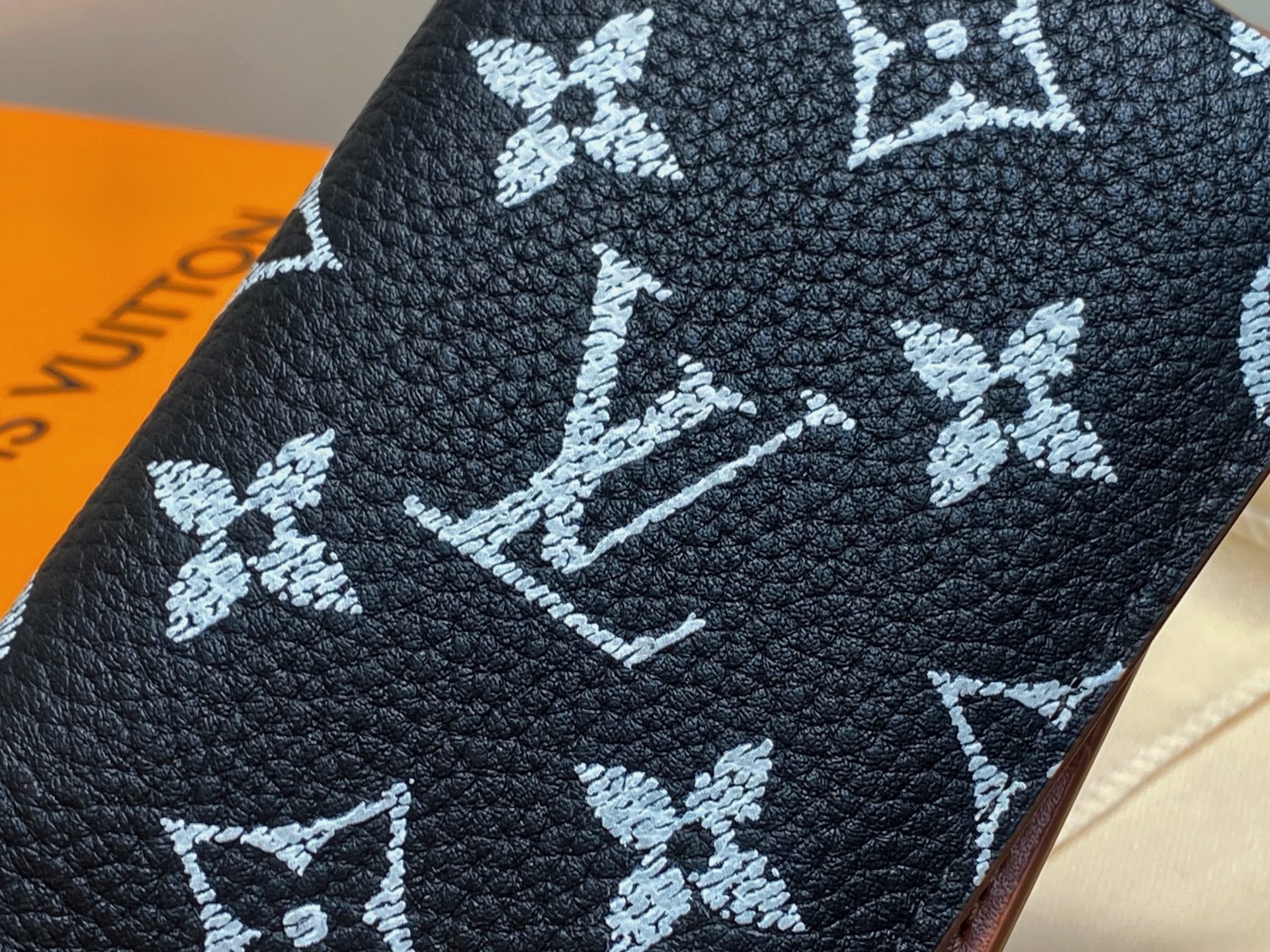 Small navy wallet with white monogram floral pattern, leather-grain close-up