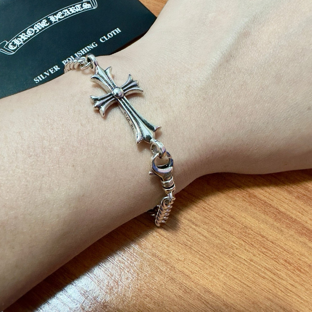 Silver-tone cross charm bracelet on wrist with chain and ring clasp
