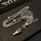 Silver-tone chain necklace with dagger and fleur de lis charms on dark jewelry box