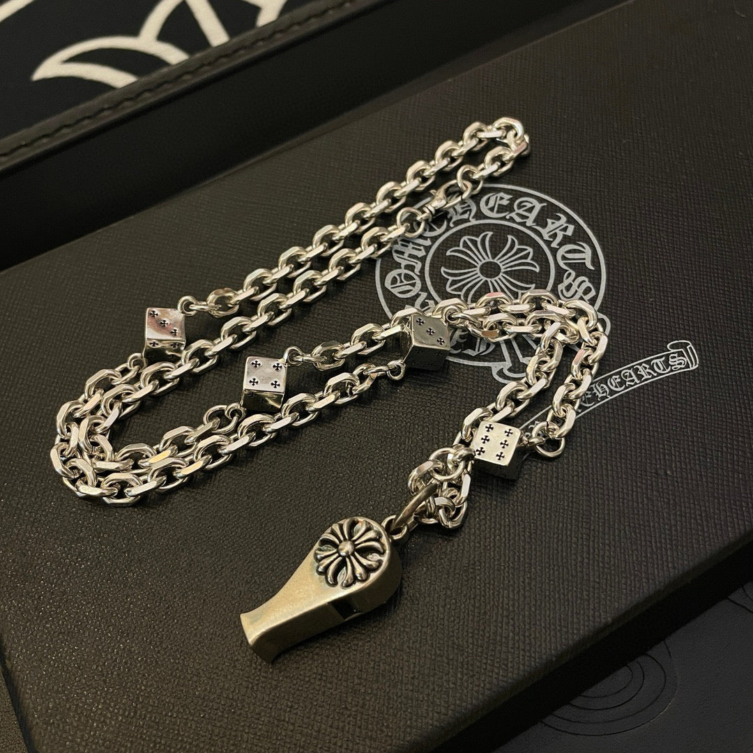 Silver-tone chain necklace with dagger and fleur de lis charms on dark jewelry box
