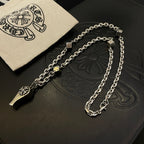 Silver-tone chain necklace with fleur de lis and dagger charms with cloth pouch