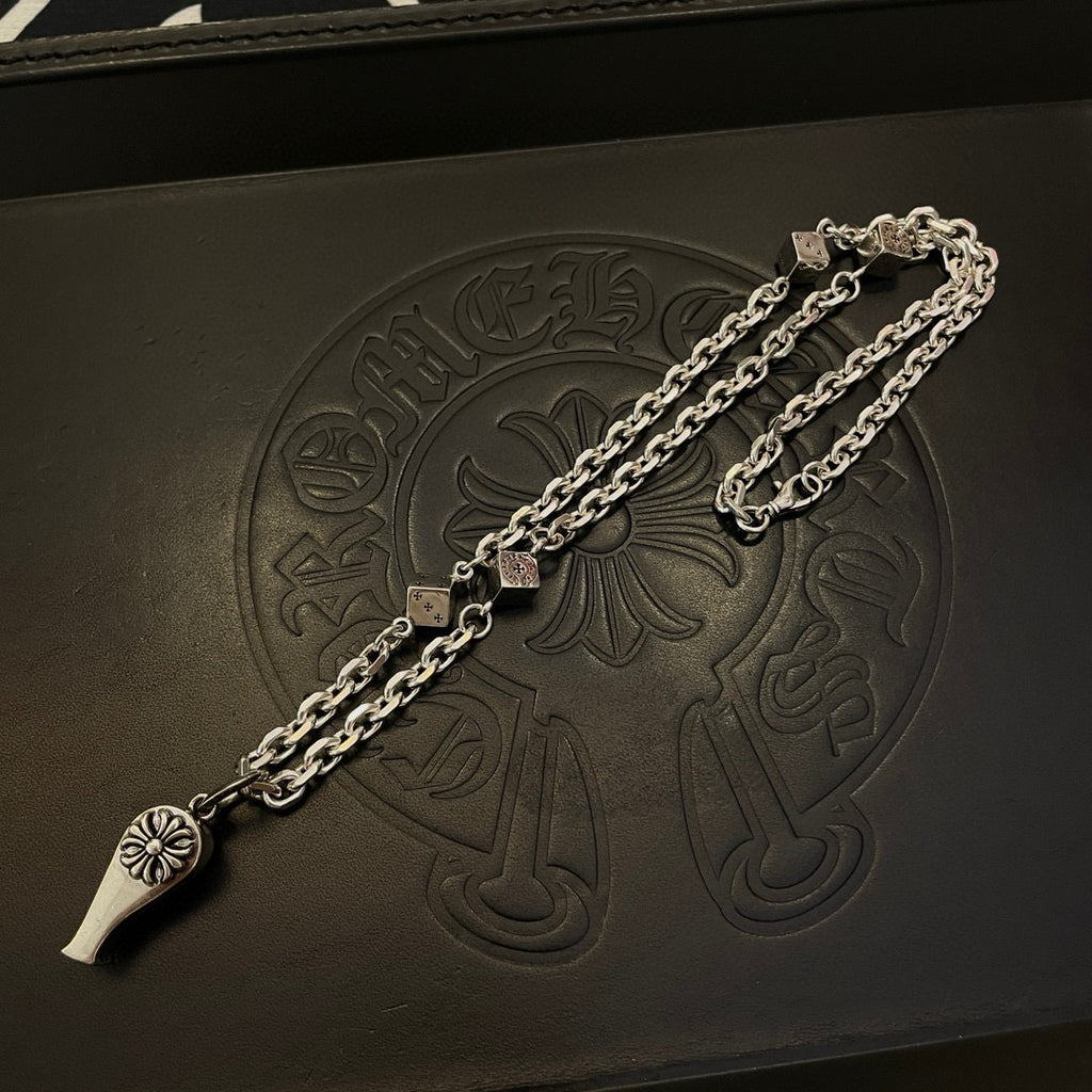 Silver-tone necklace chain on black leather jewelry box with floral emblem embossing