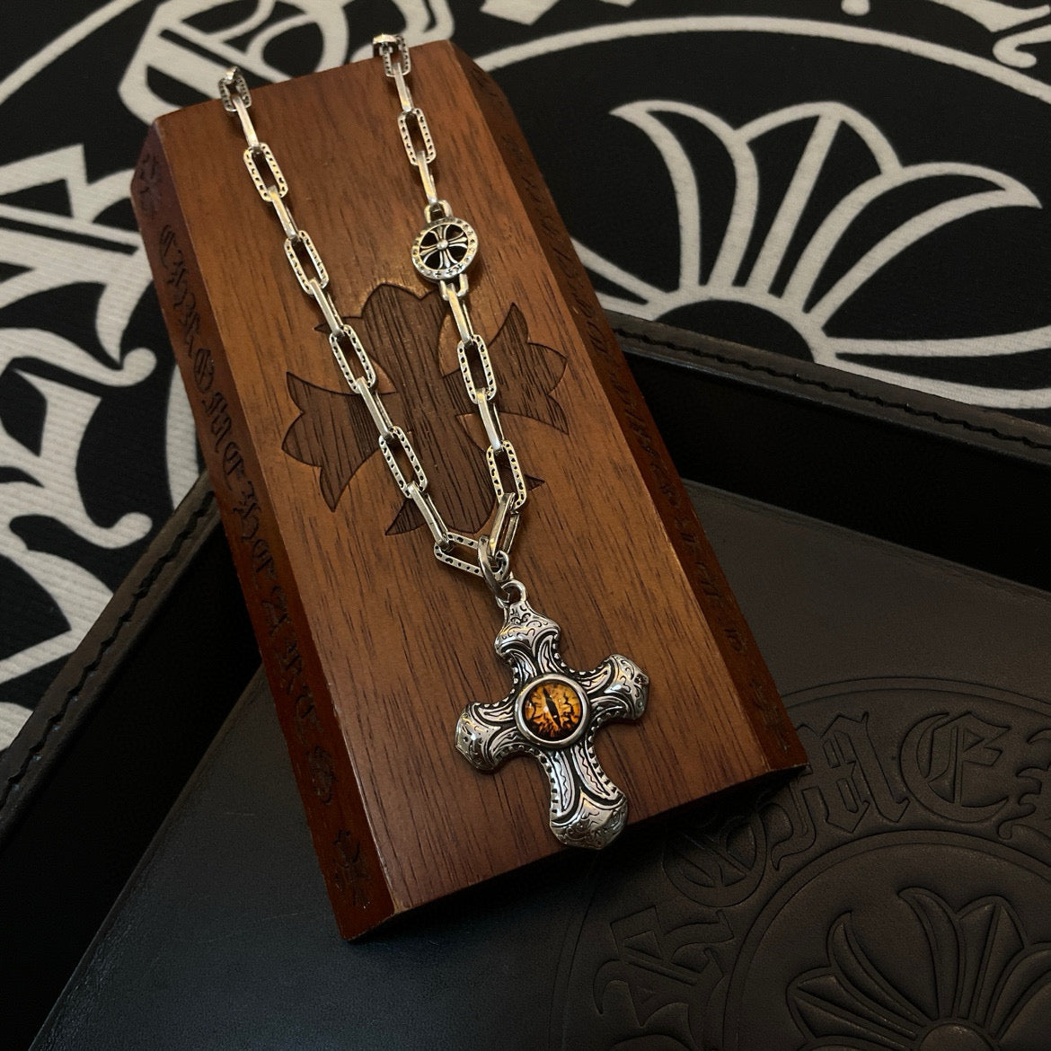 Silver-tone chain necklace with amber cross pendant on wooden display stand