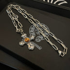 Silver-tone chain necklace with amber cross pendant on black tray