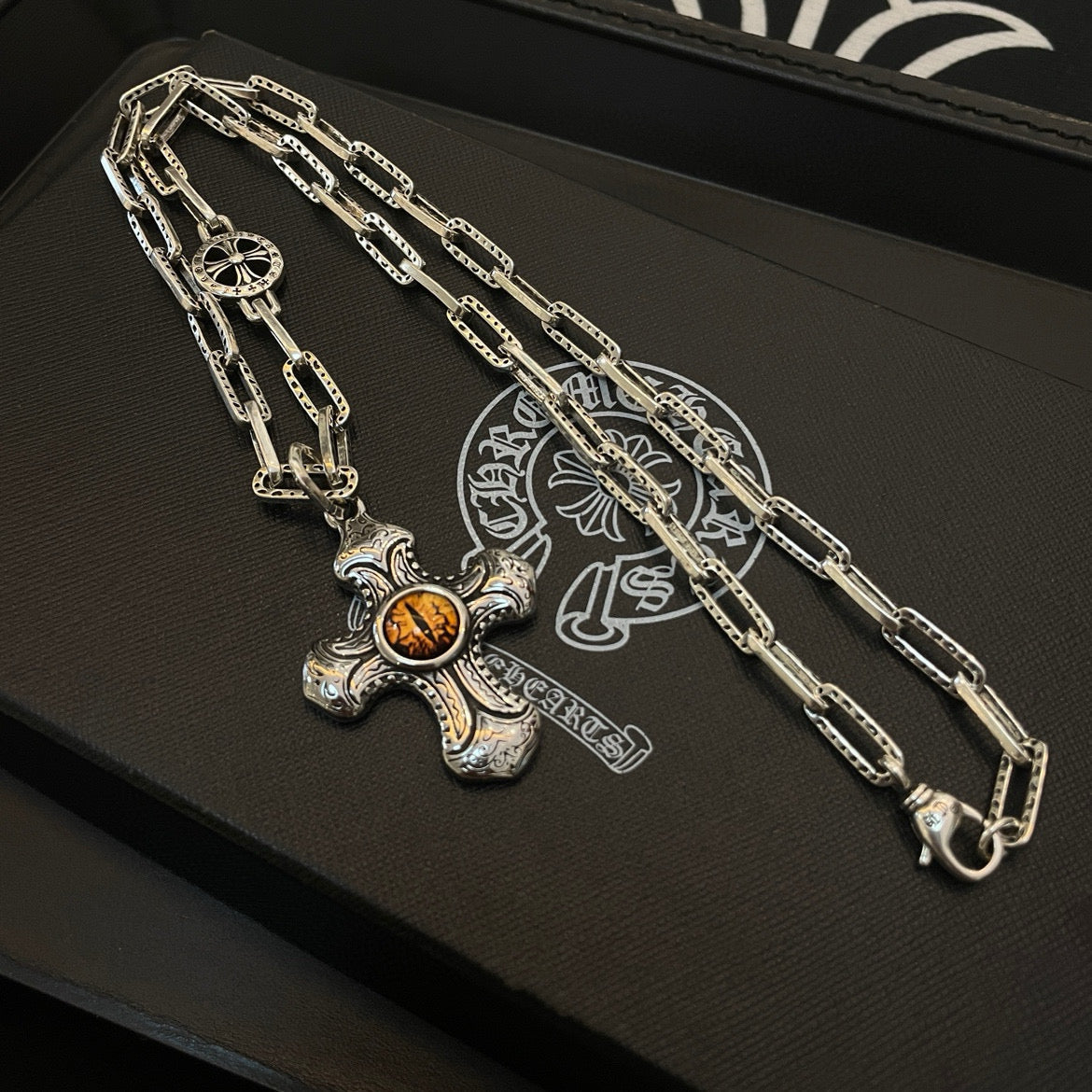 Silver-tone chain necklace with amber cross pendant on black tray