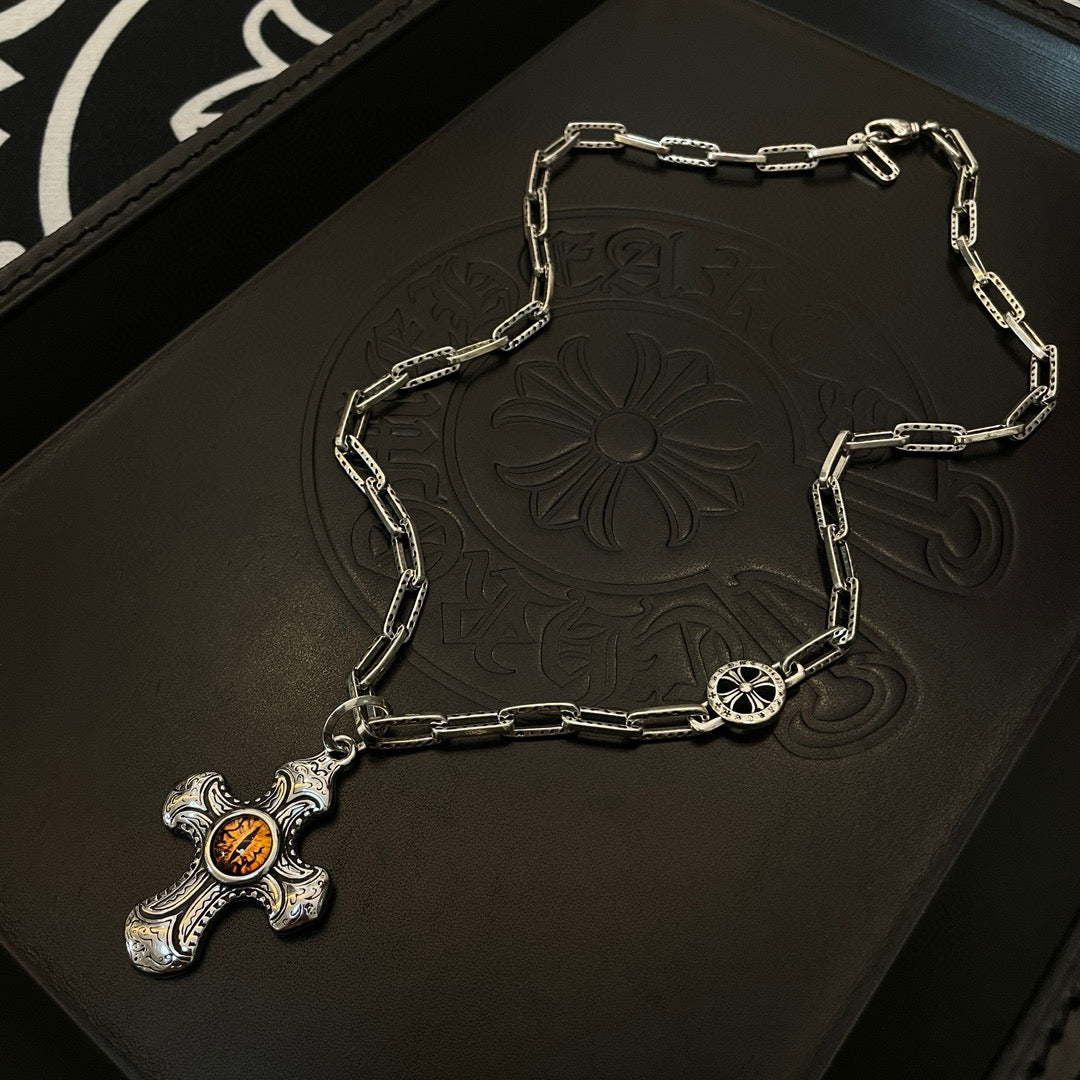 Silver-tone chain necklace with amber cross pendant on dark jewelry case