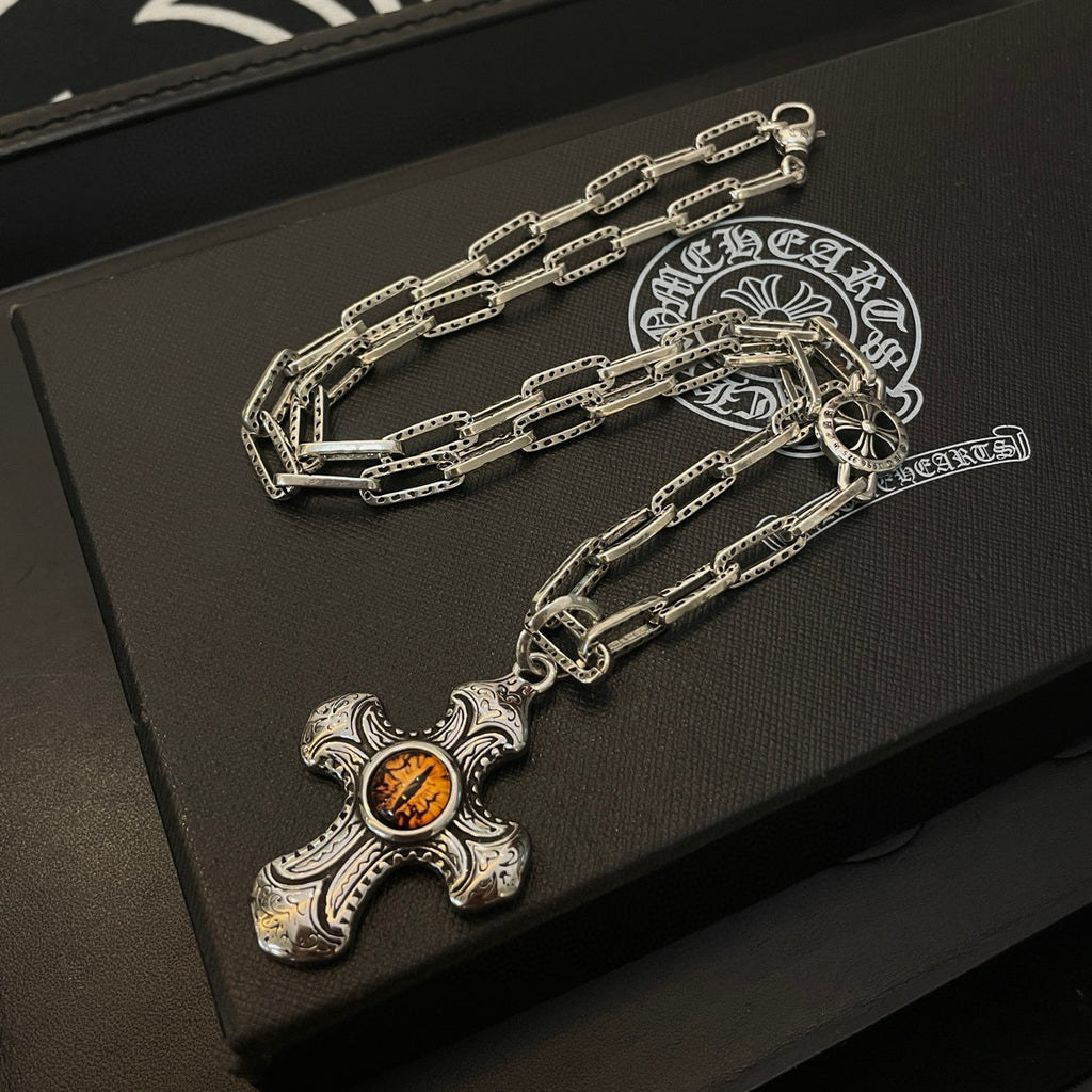 Silver-tone chain necklace with amber cross pendant and round emblem charm on box