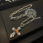 Silver-tone chain necklace with amber cross pendant and round emblem charm on box
