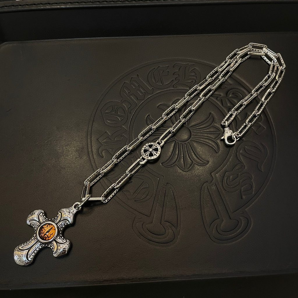Silver-tone chain necklace with amber cross pendant on dark jewelry box