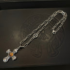 Silver-tone chain necklace with amber cross pendant on dark jewelry box