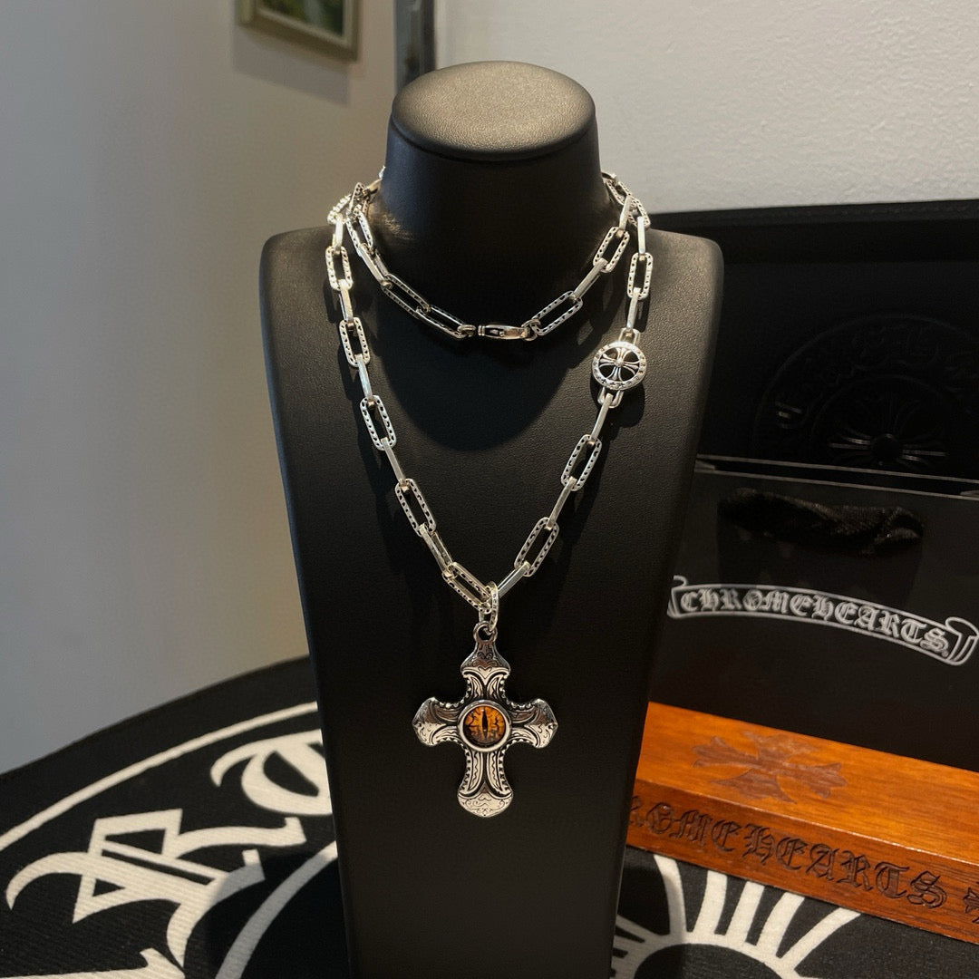 Silver-tone chain necklace with amber cross pendant and round charm on stand