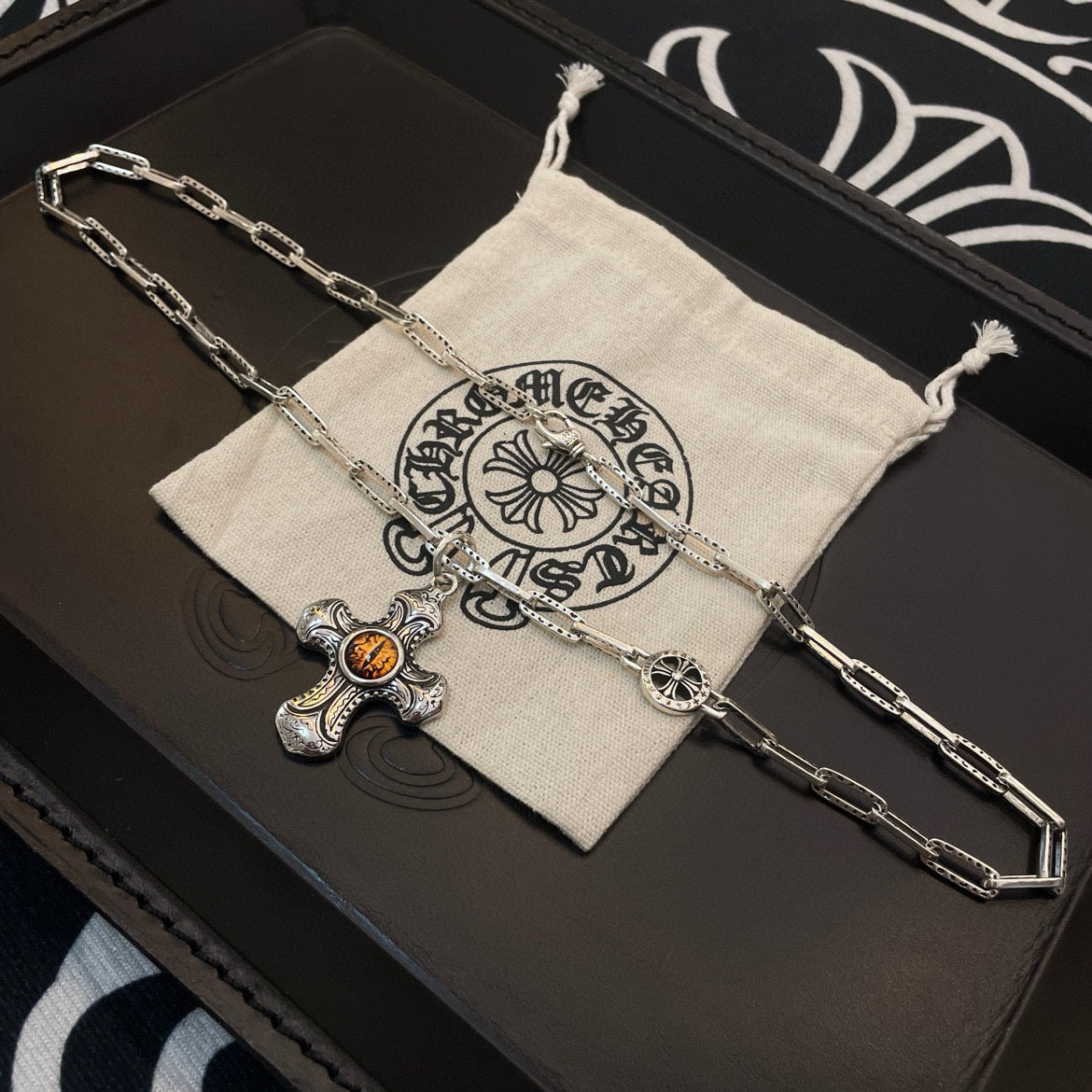 Silver-tone chain necklace with amber cross pendant on beige drawstring pouch