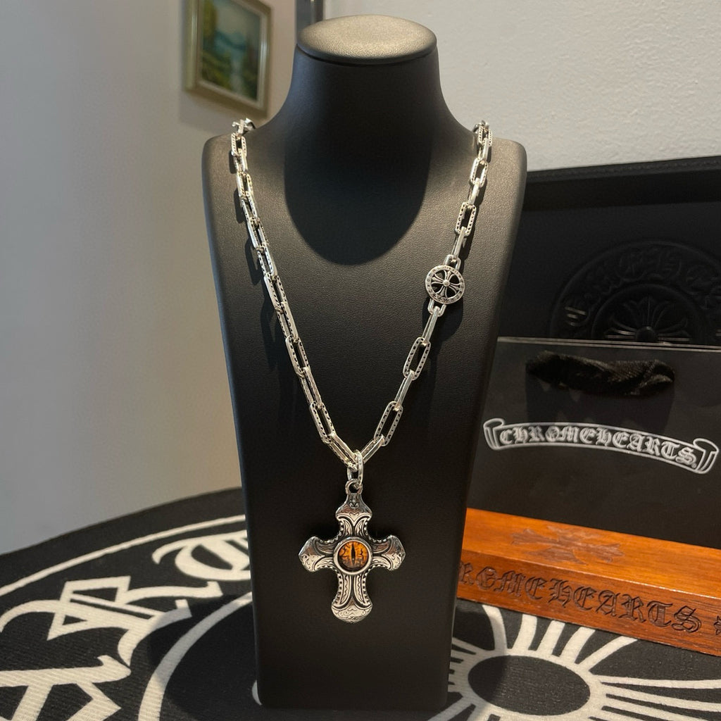 Silver-tone chain necklace with amber cross pendant and round emblem charm on stand