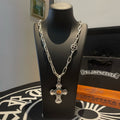 Silver-tone chain necklace with amber cross pendant and round emblem charm on stand