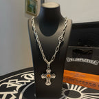 Silver-tone chain necklace with amber cross pendant and round emblem charm on stand