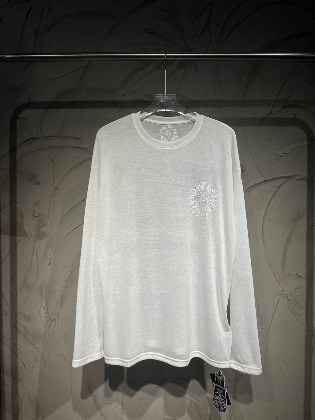White long-sleeve shirt with small crest logo on upper right chest.