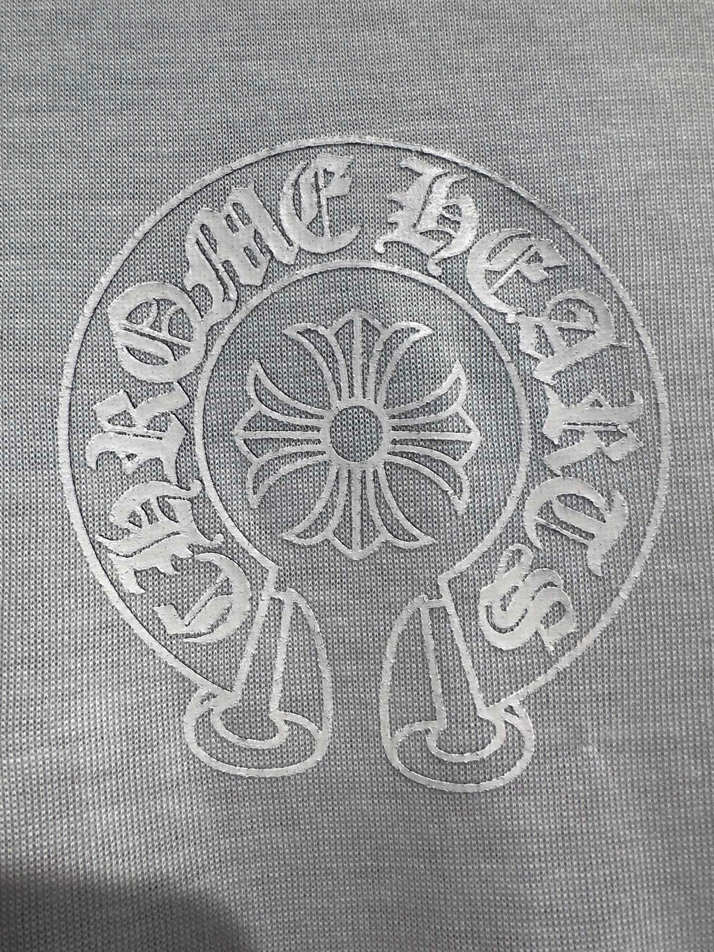White long-sleeve shirt close-up of circular crest logo with central flower motif.
