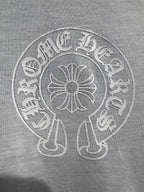 White long-sleeve shirt close-up of circular crest logo with central flower motif.