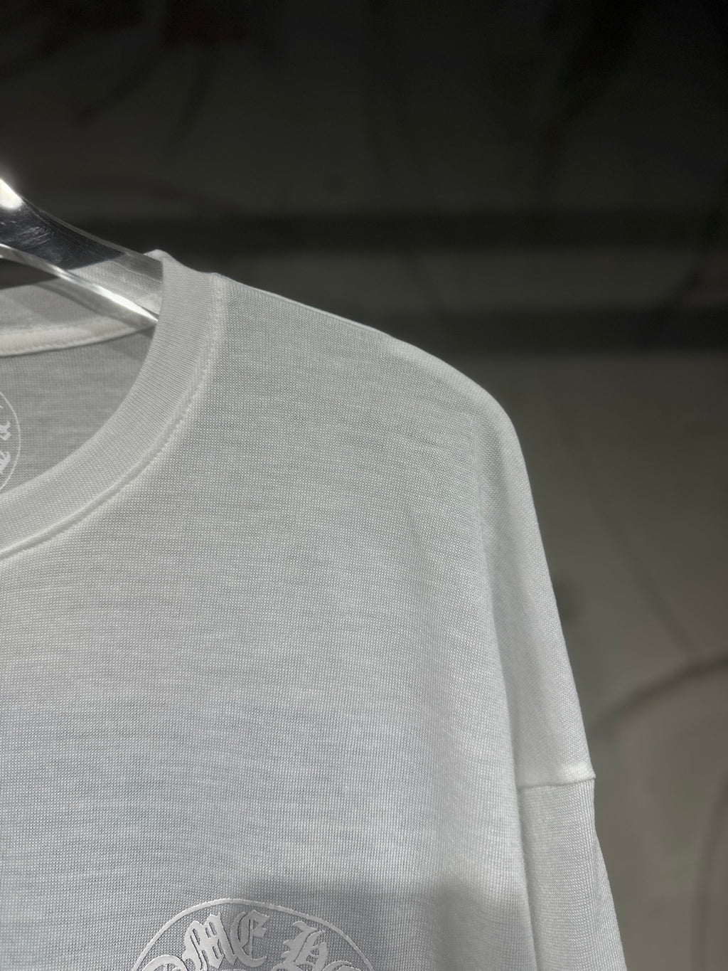 White long-sleeve shirt close-up with circular logo on lower front.