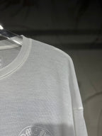 White long-sleeve shirt close-up with circular logo on lower front.