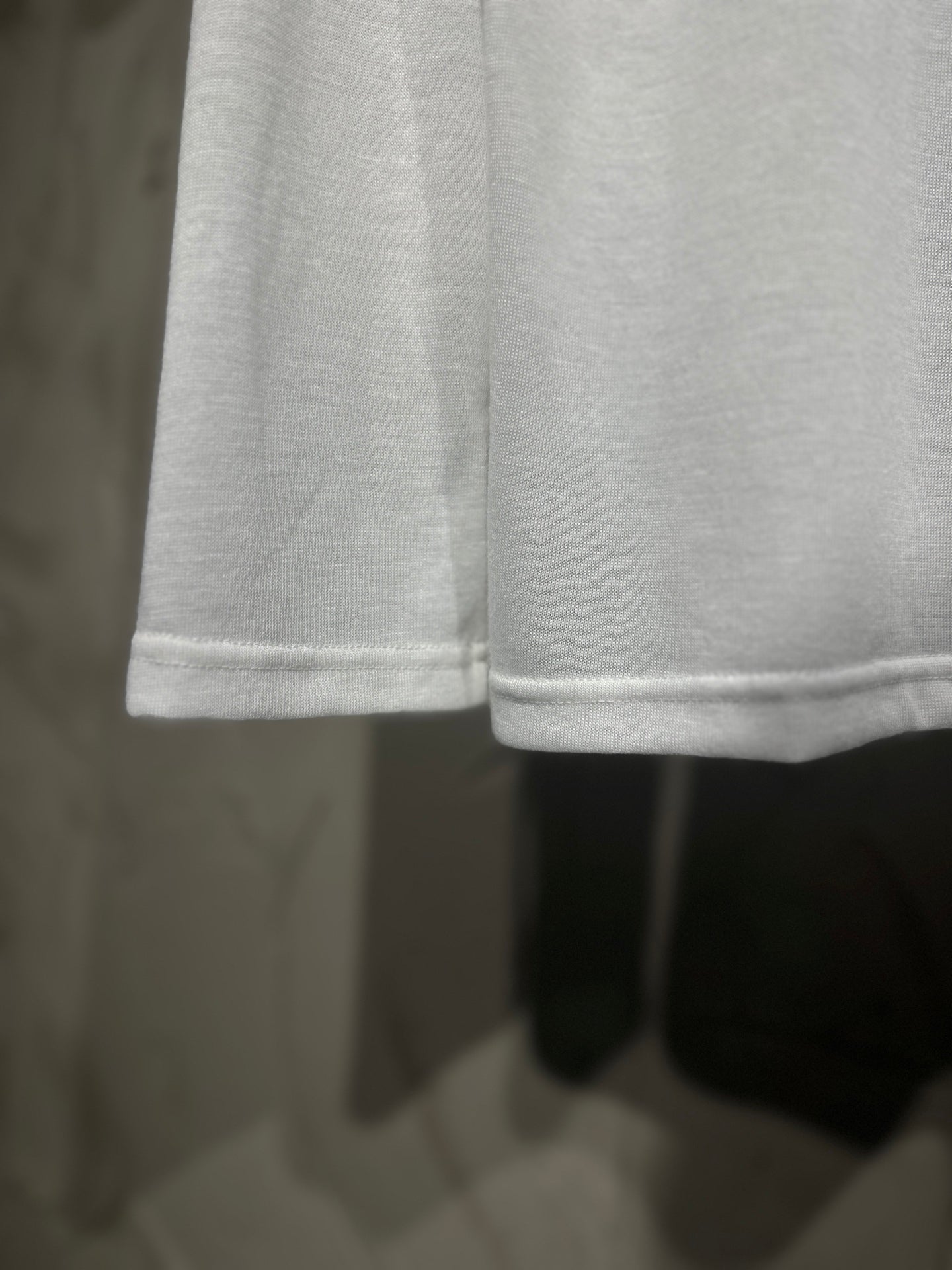 White long-sleeve shirt hem close-up with stitched sleeve cuffs.