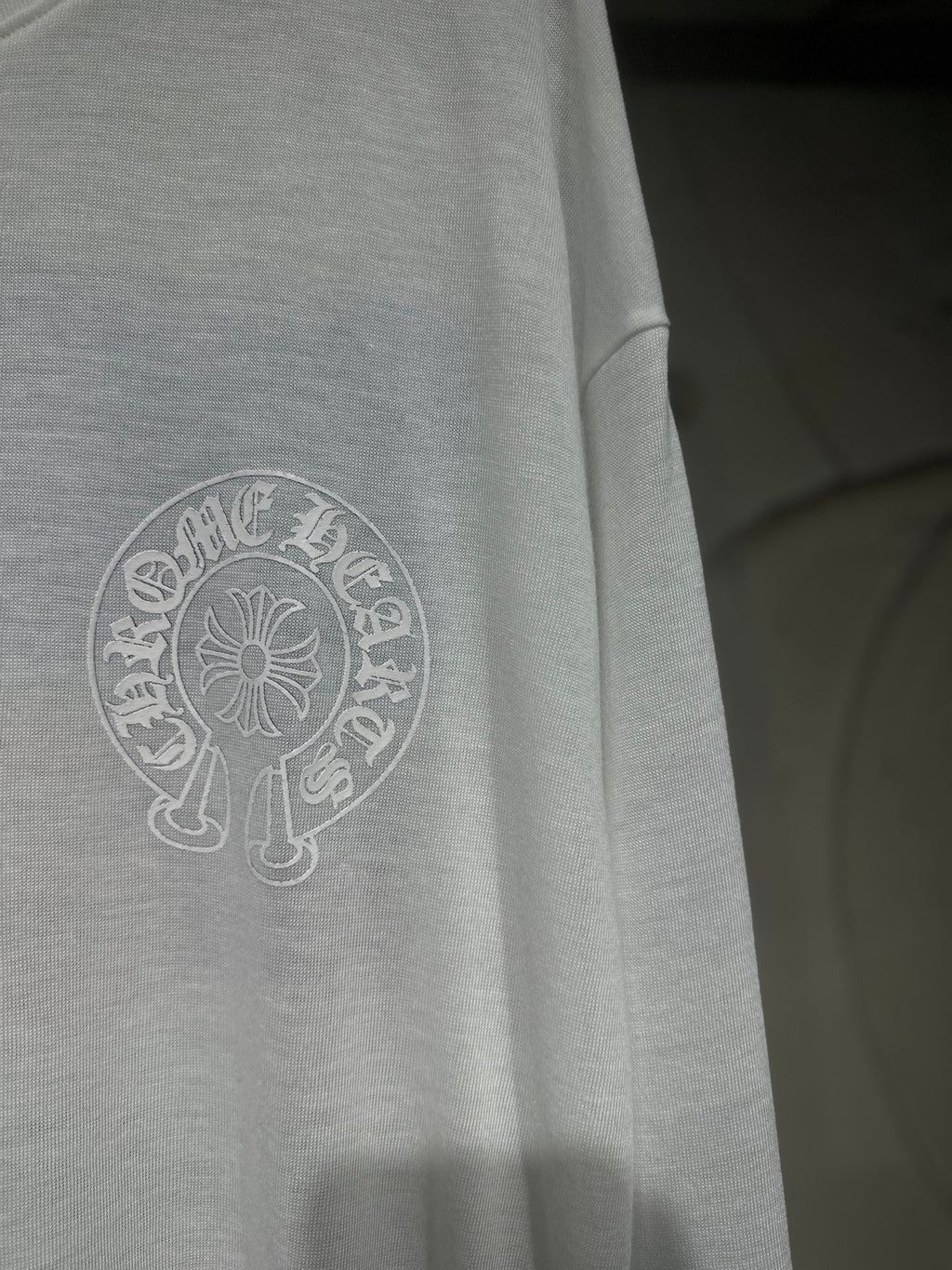 White long-sleeve shirt side close-up with circular crest logo print.