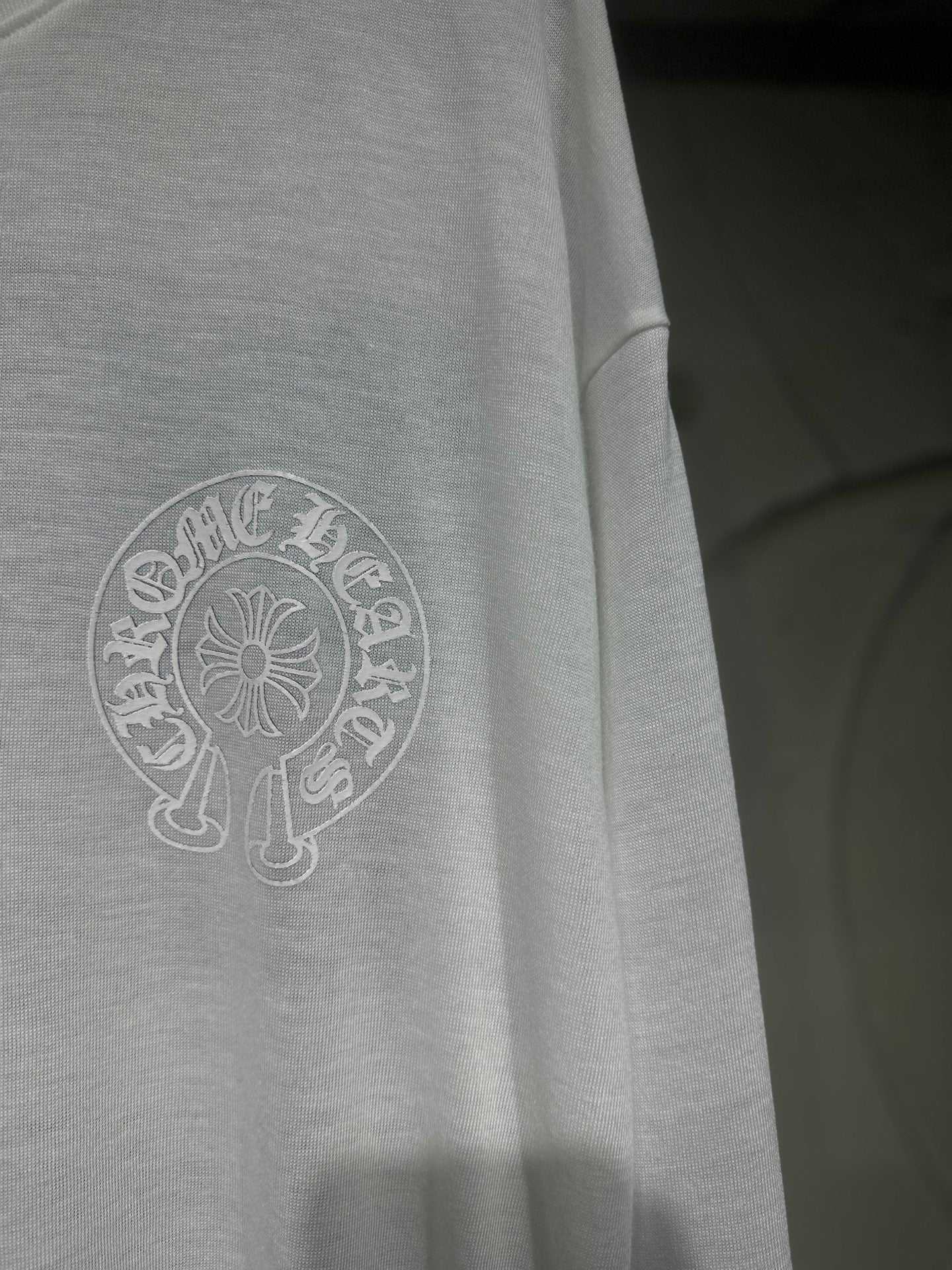 White long-sleeve shirt side close-up with circular crest logo print.