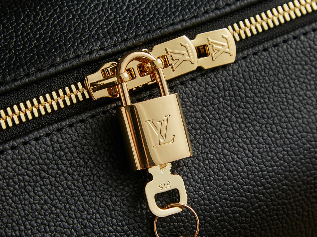 Louis Vuitton zipper pull close-up with gold hardware on black textured leather.