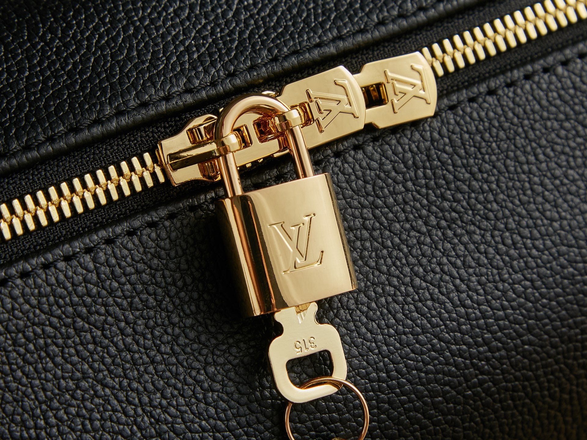 Louis Vuitton zipper pull close-up with gold hardware on black textured leather.