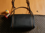 Louis Vuitton black leather handbag with top handles and buckle front pocket.