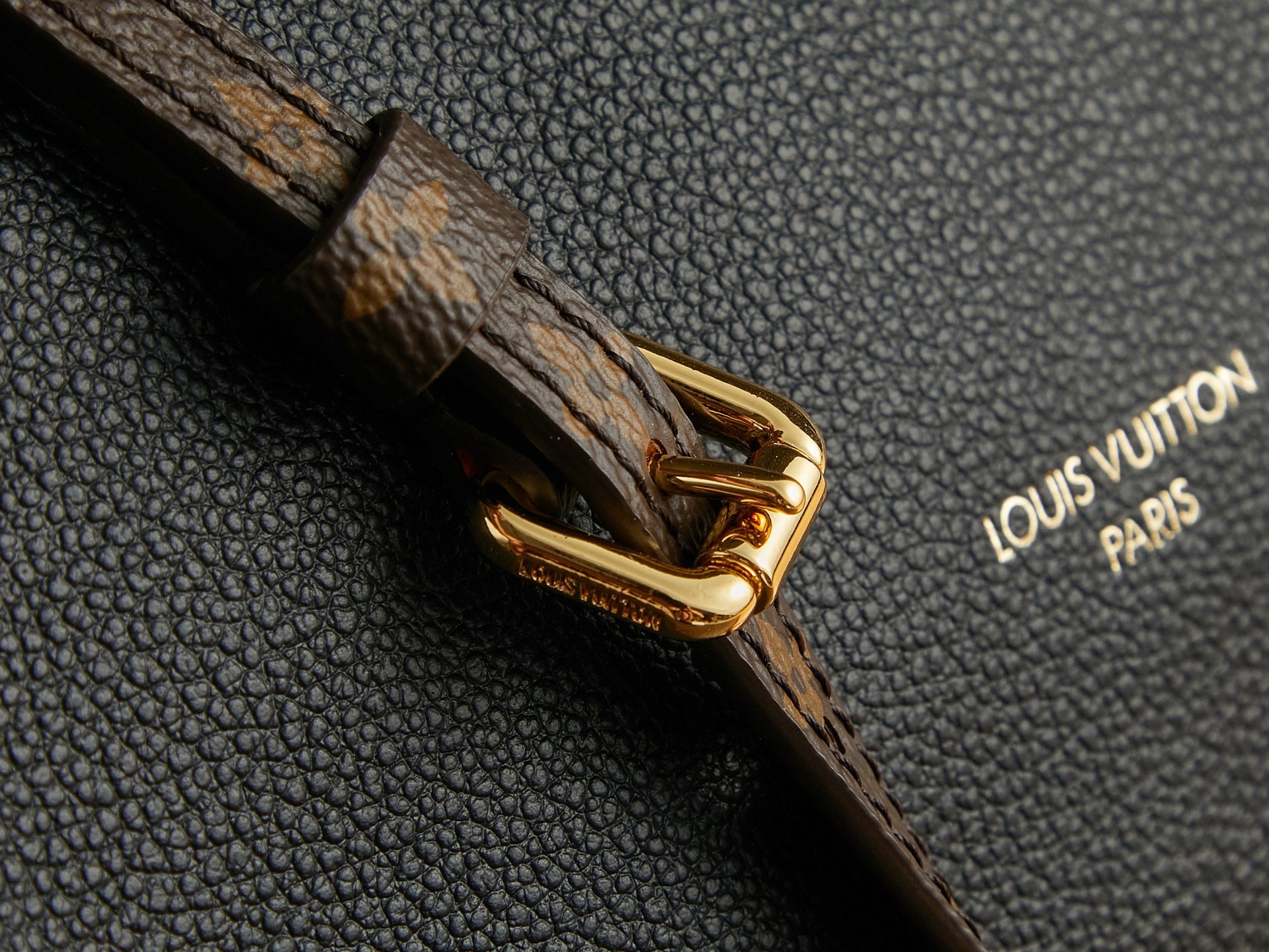 Louis Vuitton strap buckle close-up on textured black leather with brown trim.