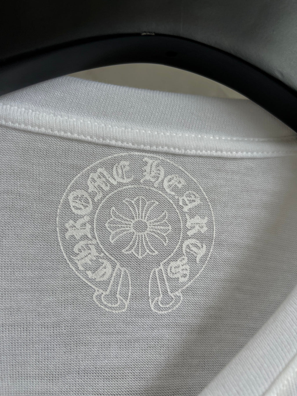 Close-up of white crewneck collar with light circular crest logo at center.