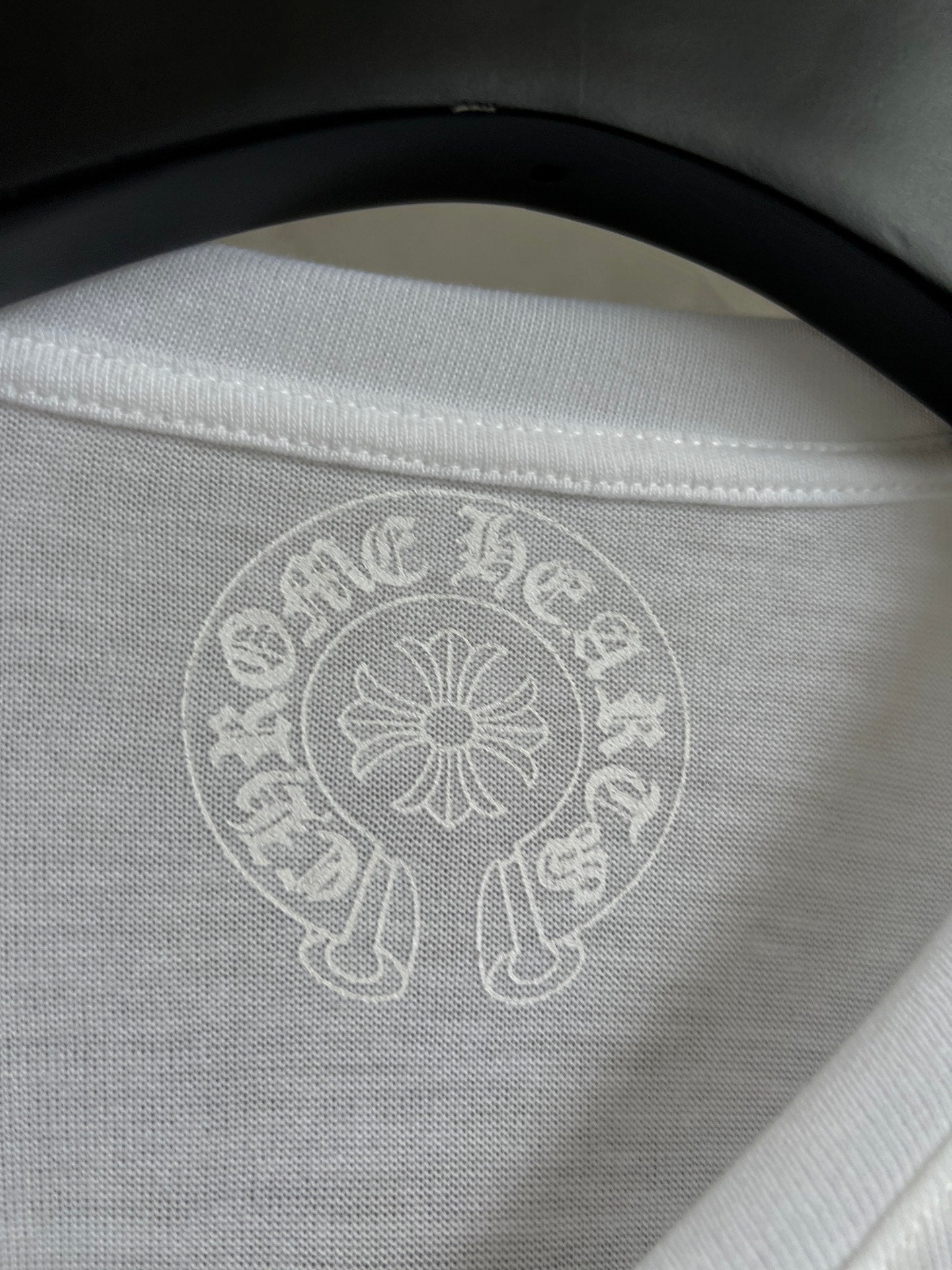 Close-up of white crewneck collar with light circular crest logo at center.