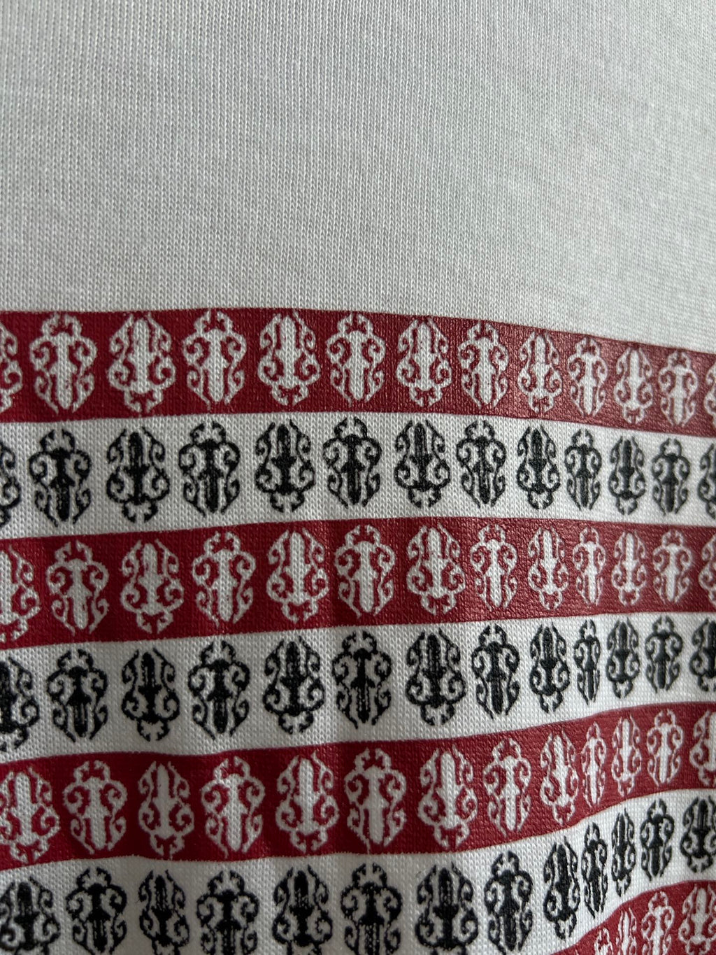 Close-up of horizontal striped graphic in black, red, and white on white shirt.