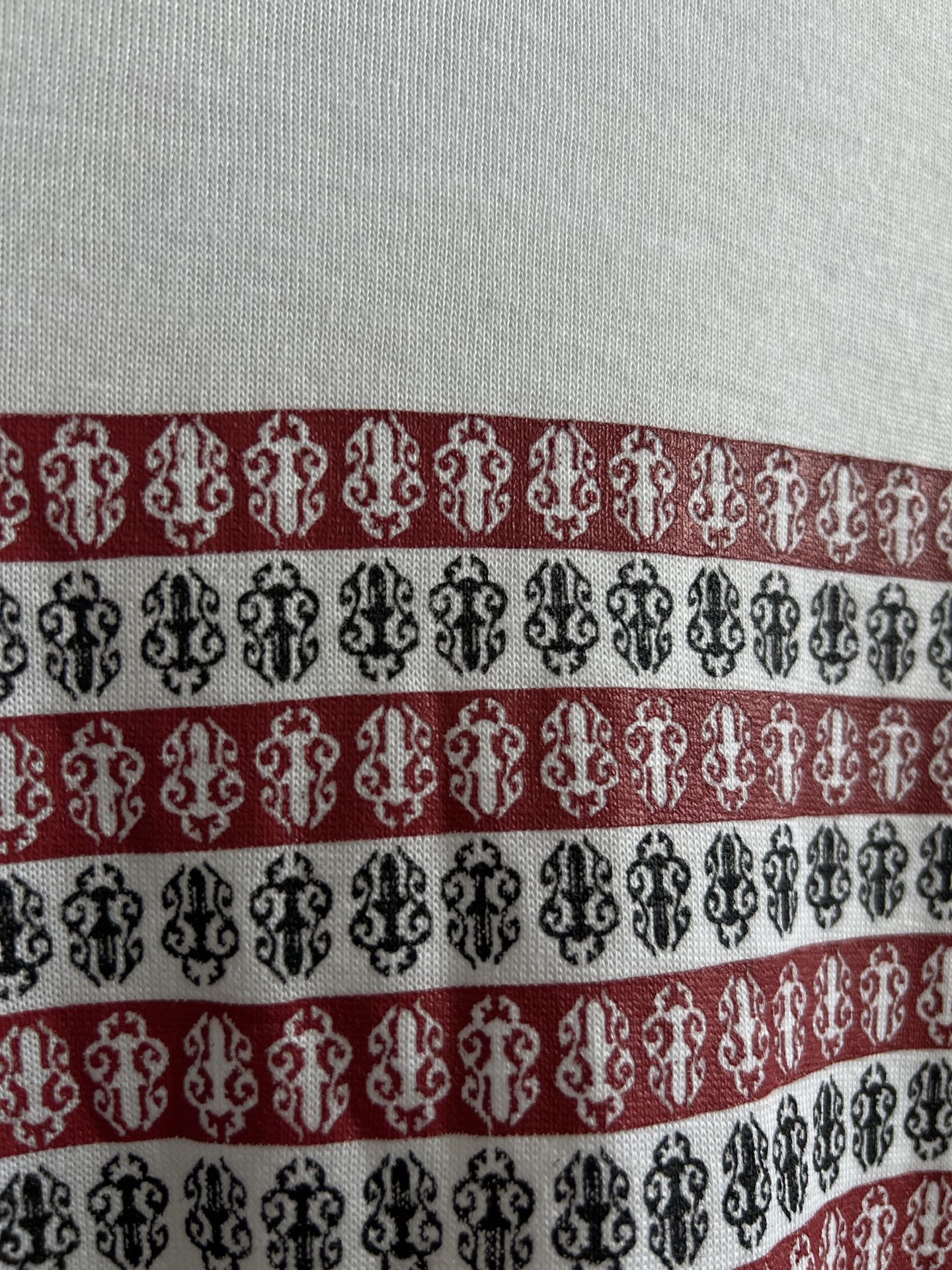 Close-up of horizontal striped graphic in black, red, and white on white shirt.