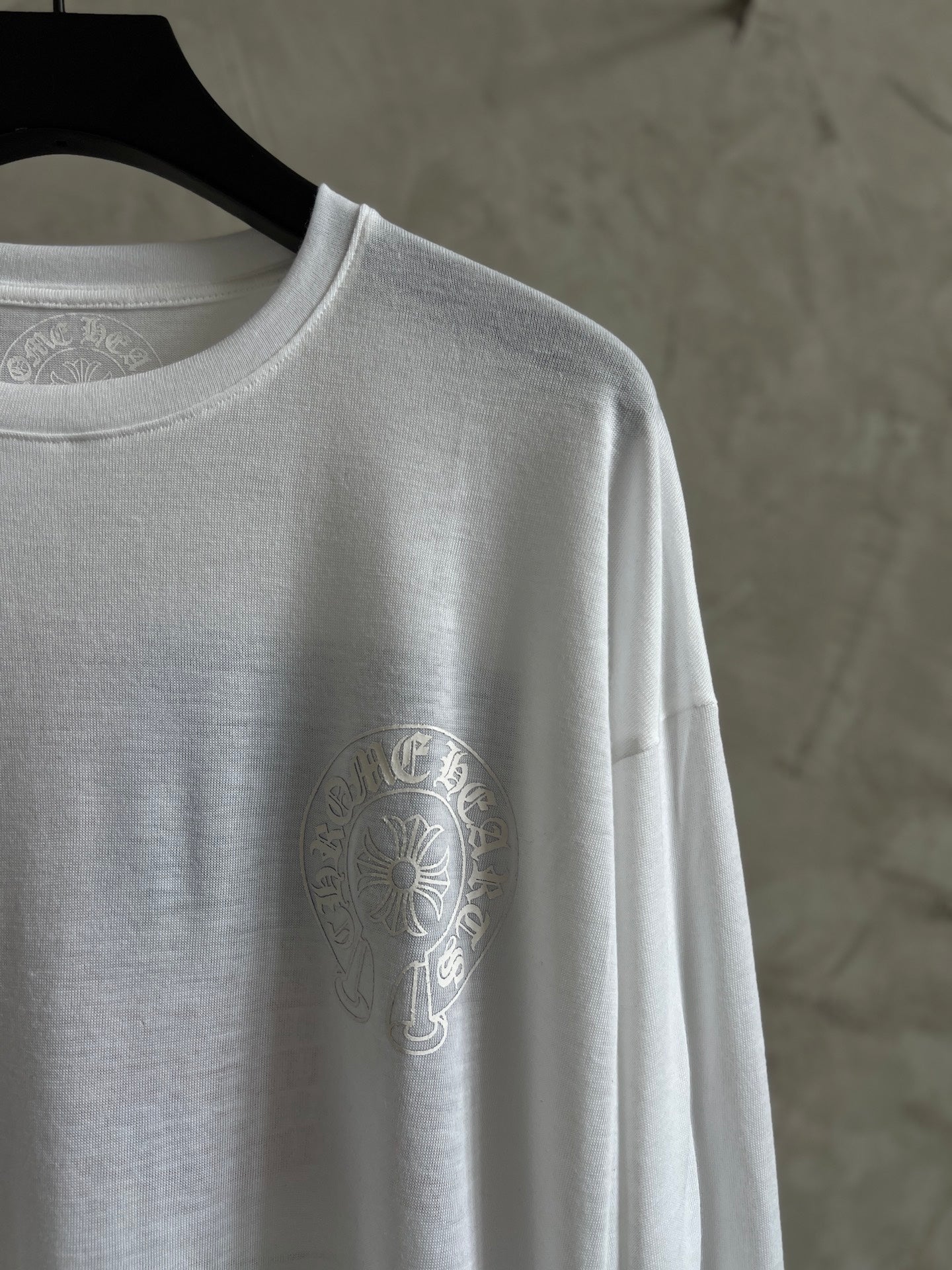 White long-sleeve shirt shoulder and left chest crest logo, crew neckline visible.