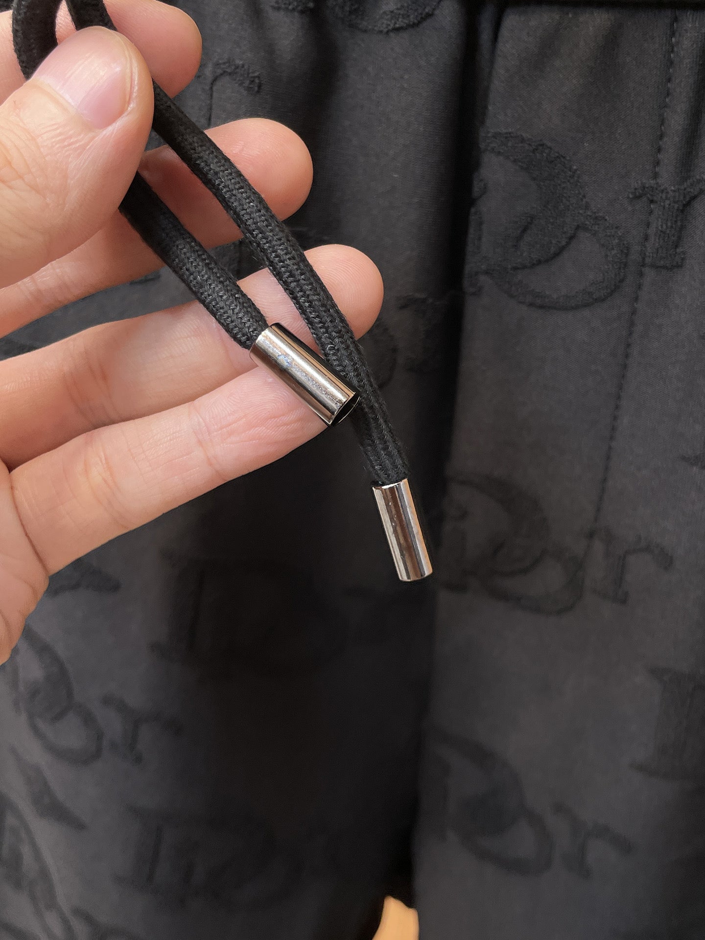 Close-up of black drawstring cords with metal aglets on Dior monogram pants