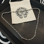 Metal chain necklace resting on black jewelry box and beige pouch