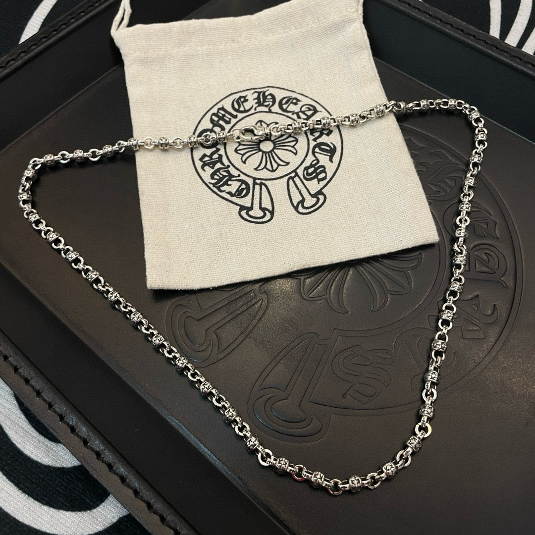 Metal chain necklace resting on black jewelry box and beige pouch