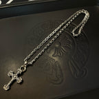 Silver-toned cross pendant necklace with layered chain, close-up on leather box