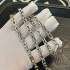 Silver-tone chain necklace stacked on white fabric cushion, multiple strands.