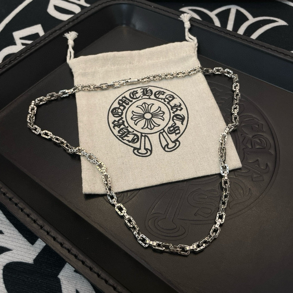 Silver-tone chain necklace coiled on leather tray with small drawstring pouch.