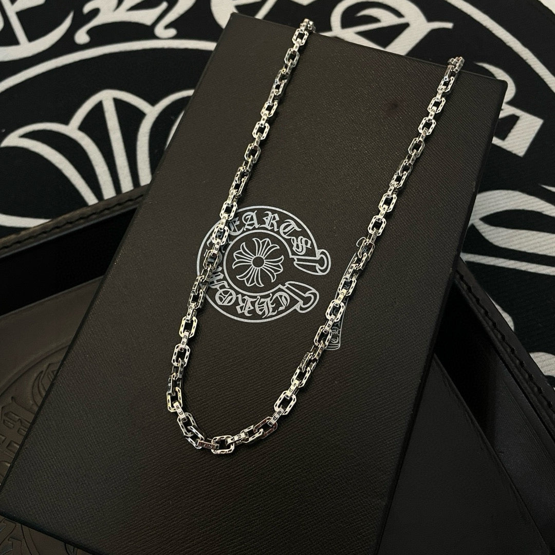 Silver-tone chain necklace on black jewelry card, round logo pendant.